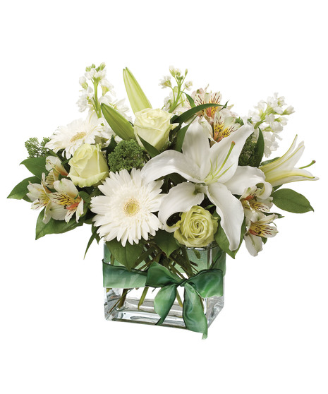 Single white oriental lily surrounded by roses, gerbera daisies, alstromeria and stock in hues of white and green in a clear glass vase.