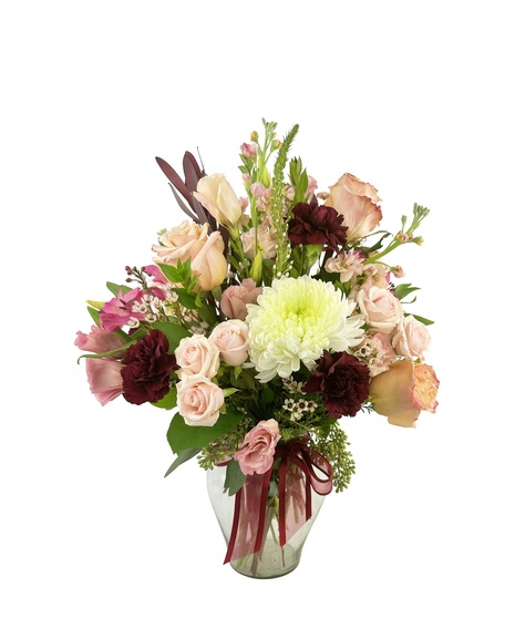 Soft hued flowers arranged in a clear vase with a wine colored ribbon.