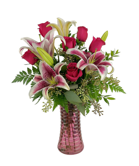 Stargazer lilies and roses are arranged in a cylinder vase with stones, wire and more. 
