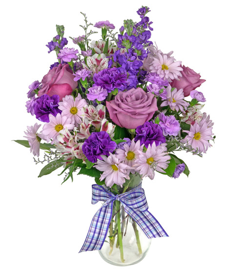 A bouquet of purple stock, mini carnations, alstromeria, and caspia in a clear glass ribbed vase and tied with a purple plaid ribbon